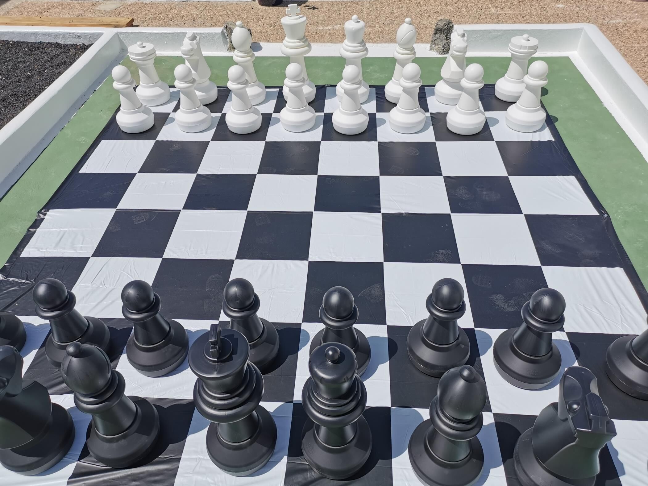 A large outdoor chessboard with black and white pieces.