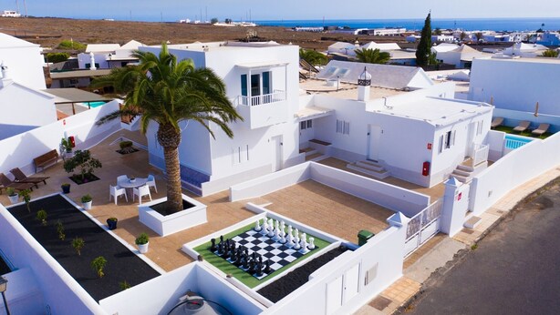 Un edificio bianco con una scacchiera sul tetto, circondato da palme e una vista libera sul mare.