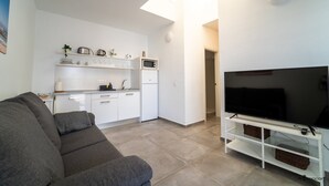 Un soggiorno moderno con un divano grigio, un televisore a schermo piatto su un mobile bianco, un angolo cottura con pensili bianchi e un forno a microonde, e un lucernario.