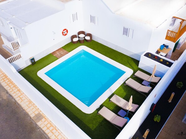 Una piscina en la azotea, de color azul, rodeada de sillones de descanso y un pequeño rincón para sentarse.