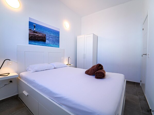 Een hotelkamer met een bed, een nachtkastje, een lamp, een kledingkast en een schilderij van een vuurtoren aan de muur.