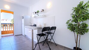 Ett modernt kök med vita skåp, ett kylskåp i rostfritt stål, en mikrovågsugn och en kaffebryggare på bänkskivan. Det finns två svarta stolar och en krukväxt.