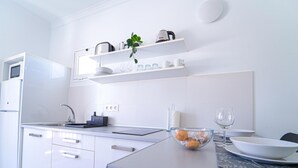 Ett modernt kök med vita skåp, en inbyggd mikrovågsugn och en bänkskiva med en skål med apelsiner och ett vinglas.