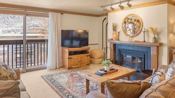 Ein Wohnzimmer mit Kamin, Fernseher und einem Balkon mit Blick auf eine verschneite Landschaft.