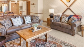 Ein Wohnzimmer mit zwei Ledersofas, einem Holztisch, gemusterten Teppichen und einer Wandleuchte.