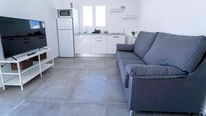 A modern living room with a flat-screen TV, grey sofa, white cabinetry, and a compact kitchen area. - Two bedroom apartment with double beds (TAHICHE)