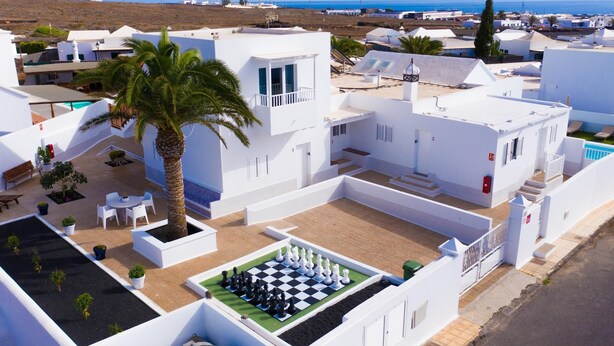A residential area with white buildings, a palm tree, and a chessboard in the courtyard. - Two bedroom apartment with double beds (TAHICHE)