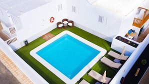 Una piscina en la azotea, de color azul, rodeada de sillones de descanso y un pequeño rincón para sentarse.