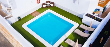 Ein Pool auf dem Dach mit blauem Wasser, umgeben von Liegestühlen und einer kleinen Sitzecke.