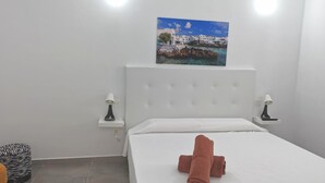 Habitación de hotel con cama, dos mesitas de noche con lámparas, un reposapiés con estampado de cebra y un cuadro de una escena costera.