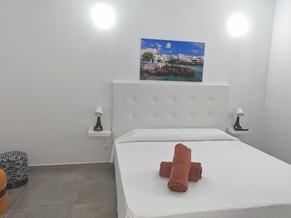 A hotel room with a bed, two bedside tables with lamps, a zebra-patterned ottoman, and a painting of a coastal scene.