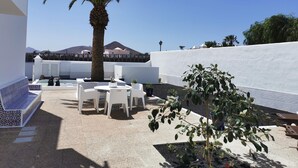 Une terrasse avec des meubles blancs, un palmier et une vue sur une montagne.