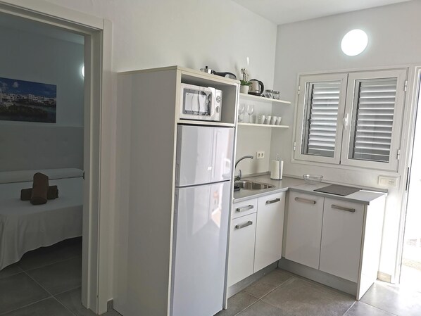 A modern kitchen with white cabinetry, a built-in oven, and a window with blinds. - Two bedroom apartments with double beds. (TAHICHE)