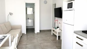 Una habitación moderna y bien iluminada con sofá, una mesita, televisor, microondas y baño visible a través de una puerta abierta.