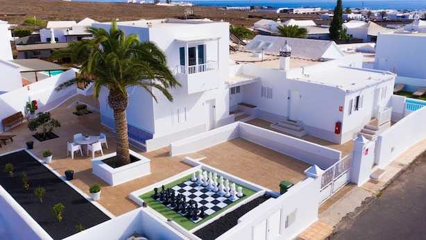 Zona residencial con edificios blancos, una palmera y un tablero de ajedrez en el patio.