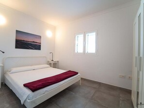 Een slaapkamer met een bed, nachtkastje, wandlamp, raam en een schilderij.