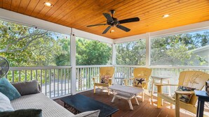 Eine überdachte Veranda mit Holzboden, Deckenventilatoren und Sitzbereichen mit Sesseln und einer Couch.