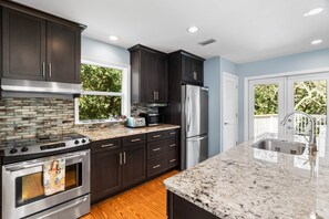 A modern kitchen with dark cabinets, granite countertops, stainless steel appliances, and a large window overlooking greenery. - Stella Luna in Old Grayton- Perfect for Families and Friends (Walton County)
