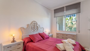 Une chambre avec un grand lit, une table de chevet avec une lampe, une commode et une fenêtre donnant sur un paysage verdoyant.