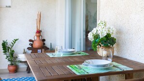 Une table en bois, mise avec des assiettes, des couverts et un verre, agrémentée d’une plante en pot et d’un vase de fleurs.