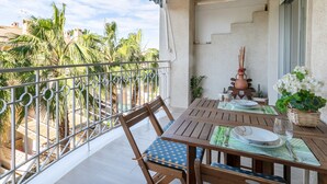 Un balcon avec une table dressée pour le repas, des chaises, une balustrade et une vue sur des palmiers et des immeubles.