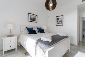 A bedroom with a bed, nightstand, lamps, and framed pictures on the wall.