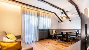 Una sala de estar moderna con sofá, mesa de comedor, sillas, televisor y un ventanal con cortinas.