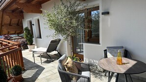 Un patio con mobiliario exterior, un árbol en maceta y una botella sobre una mesa.