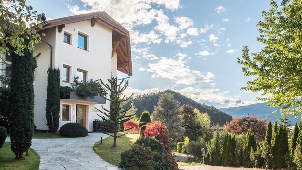 A modern two-story house with a stone pathway leading to the entrance, surrounded by lush greenery and a mountainous backdrop. - Apartment 'Residence Skutial - Schlern' with Mountain View, Balconies & Wi-Fi (Castelrotto)