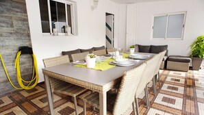 Un comedor con una mesa dispuesta para seis personas, rodeada de sillas de mimbre, un suelo estampado y una planta en maceta.