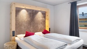 Un letto matrimoniale con testiera in legno, due cuscini rossi e un comodino con uno sgabello in legno.