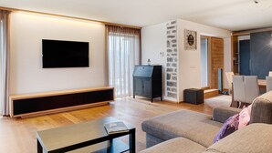 Un salon moderne doté d’un téléviseur à écran plat, d’un meuble de rangement noir, d’un canapé et d’un coin repas avec des chaises.