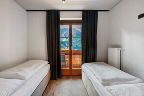 A room with two single beds, a wooden floor, a window with curtains, and a view of mountains. - Apartment "Angerle Alm Apt Rosengarten" with Private Balcony, Shared Garden and Wi-Fi (carezza Nova Levante)