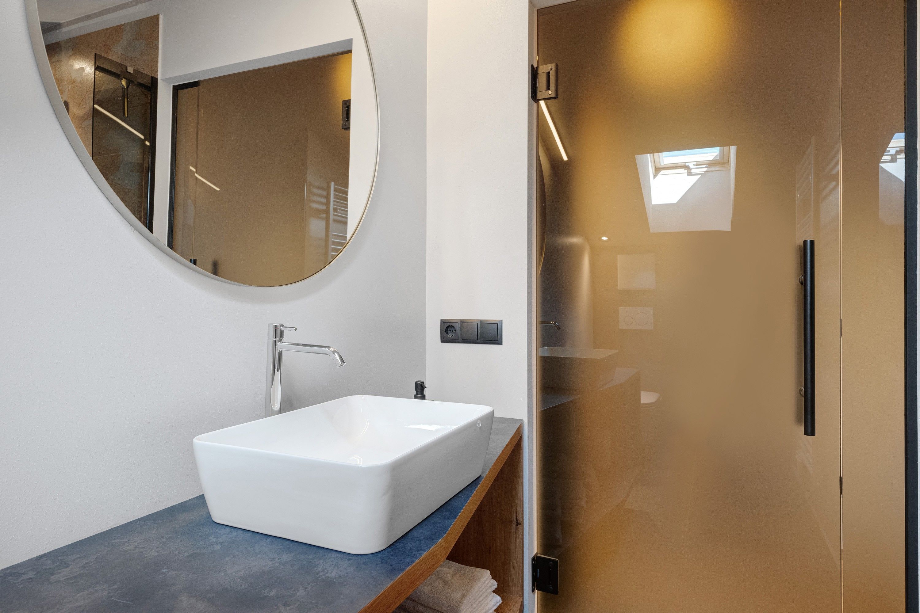 Ein modernes Badezimmer mit einem großen, ovalen Spiegel, einem rechteckigen weißen Waschbecken und einer Duschkabine aus Glas.