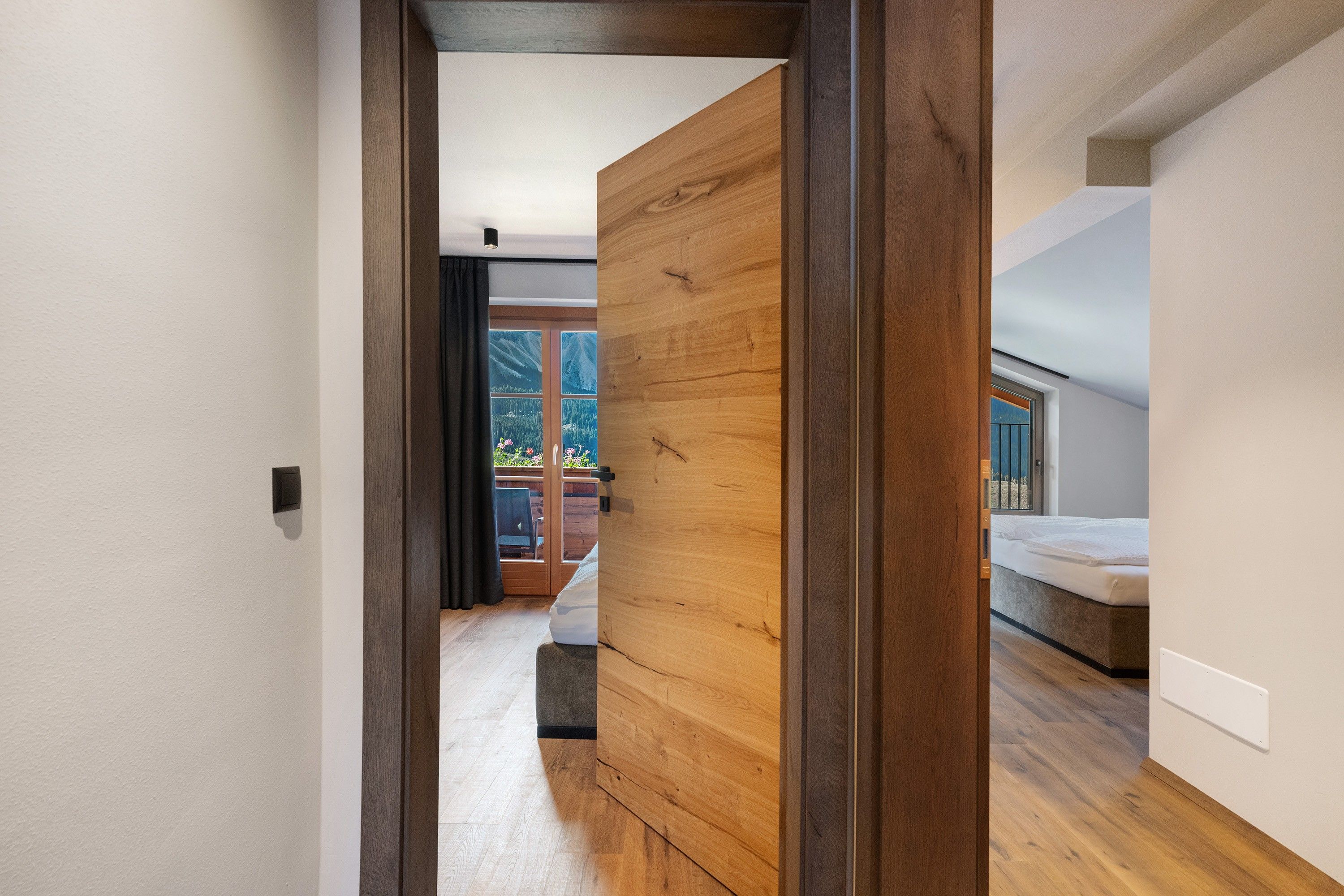A modern interior with a wooden door leading to a balcony with a view of mountains.