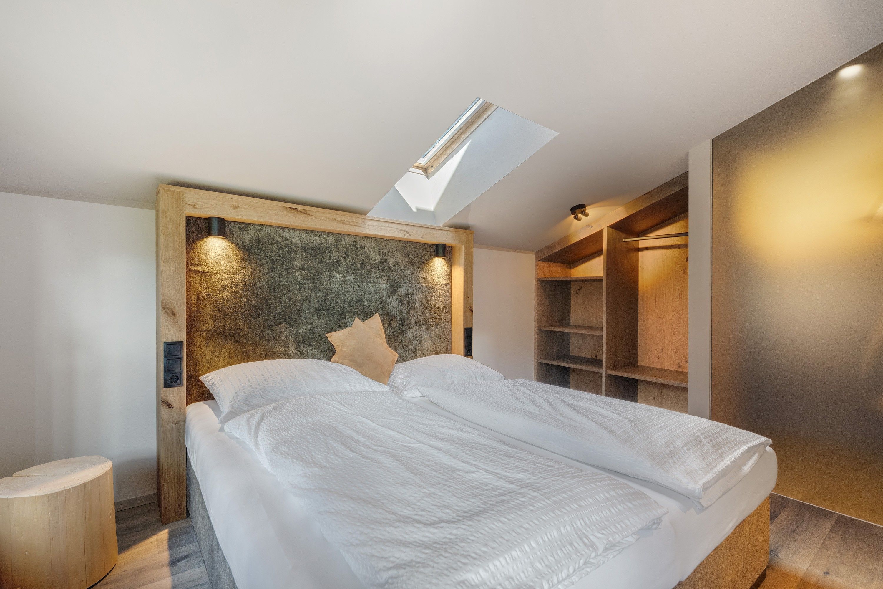 Une chambre à coucher moderne avec un puits de lumière, une tête de lit en bois et des étagères intégrées.
