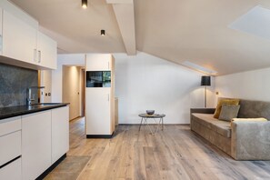 Une cuisine moderne avec des meubles blancs et un plan de travail noir, un coin repas avec une table ronde et un canapé, et un plafond doté d’un éclairage encastré.