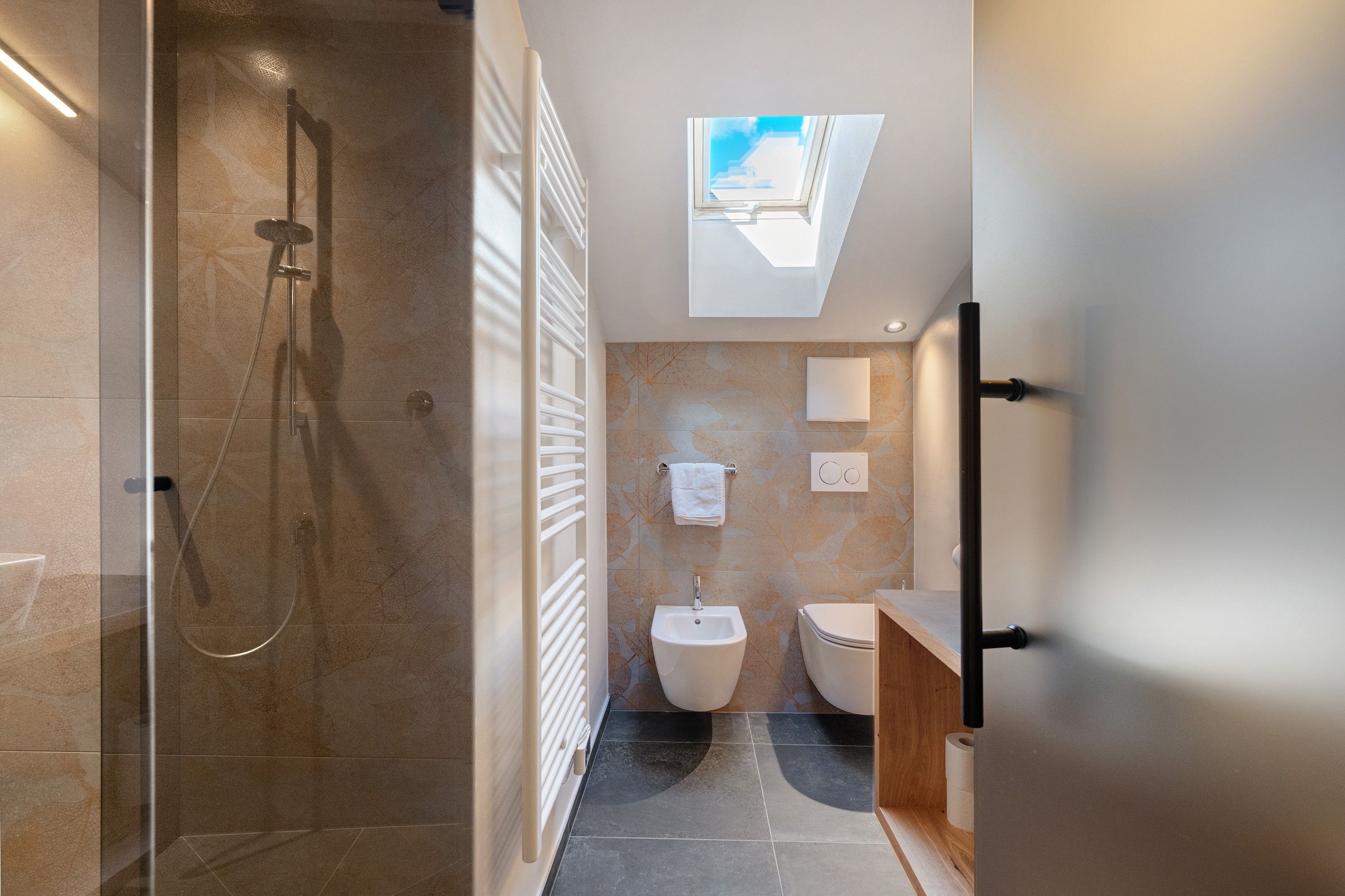 Une salle de bain moderne dotée d’une douche à parois de verre, d’un puits de lumi ère, d’un bidet et de toilettes.