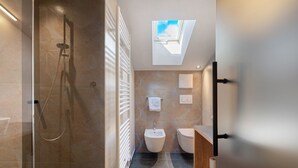 Une salle de bain moderne dotée d’une douche à parois de verre, d’un puits de lumière, d’un bidet et de toilettes.