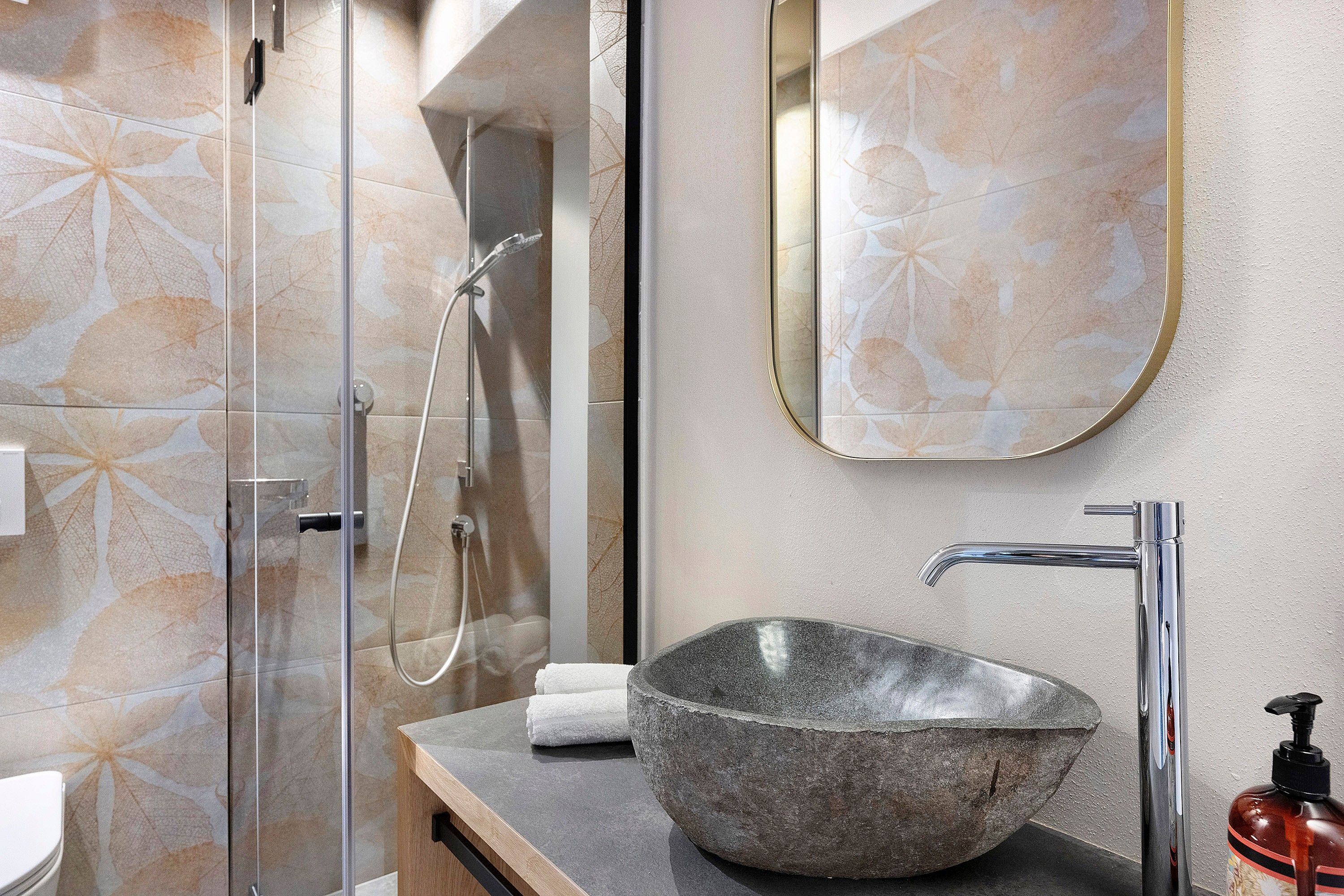 Un baño con un lavabo de piedra, un cabezal de ducha manual y un espejo.