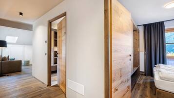 Ein modernes Interieur mit Holzboden, einer weißen Wand, einem Bett mit weißer Bettwäsche und Blick auf eine gebirgige Landschaft durch ein Fenster.