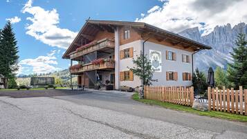 Un edificio su due piani con un balcone, una recinzione in legno e montagne sullo sfondo.