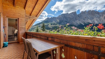 A wooden balcony with a table and chairs, overlooking a mountainous landscape with flowers.