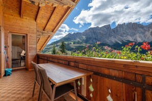 A wooden balcony with a table and chairs, overlooking a mountainous landscape with flowers. - Apartment "Angerle Alm Apt Latemar" with Private Balcony, Shared Garden & Wi-Fi (carezza Nova Levante)