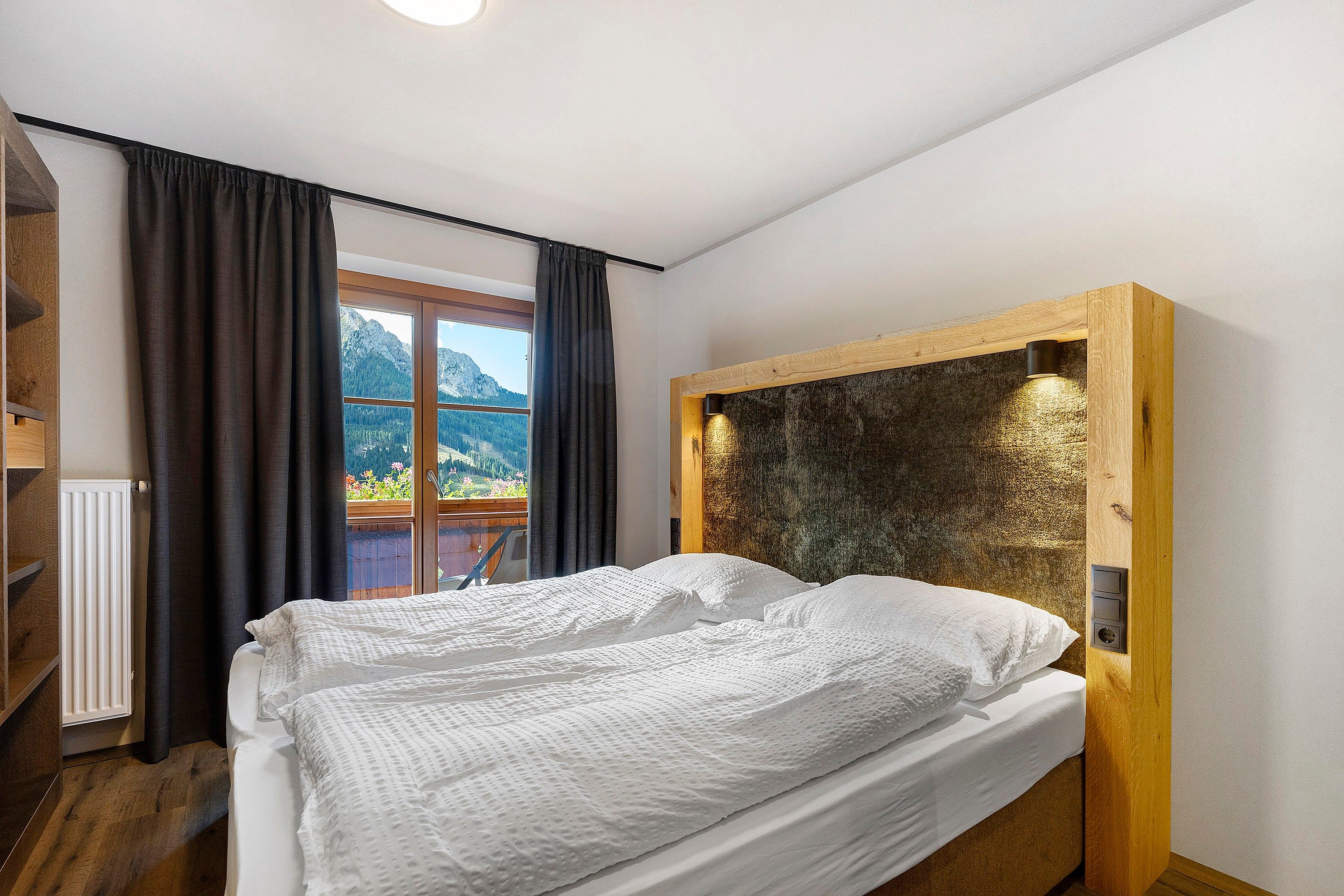 Ein Schlafzimmer mit einem Bett, einem Fenster mit Vorhängen, einem Heizkörper und einem Holz-Kopfteil.