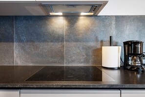 Una cocina con tope de inducción negro, cafetera y soporte para toallas de papel.