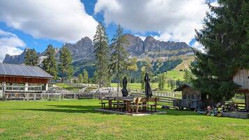 Un rifugio alpino rustico con panche e tavoli di legno in un prato, con vista su una valle e montagne sullo sfondo.
