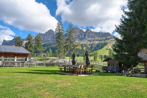 A rustic mountain lodge with wooden benches and tables in a grassy field, overlooking a valley with mountains in the background. - Apartment "Angerle Alm Apt Latemar" with Private Balcony, Shared Garden & Wi-Fi (carezza Nova Levante)