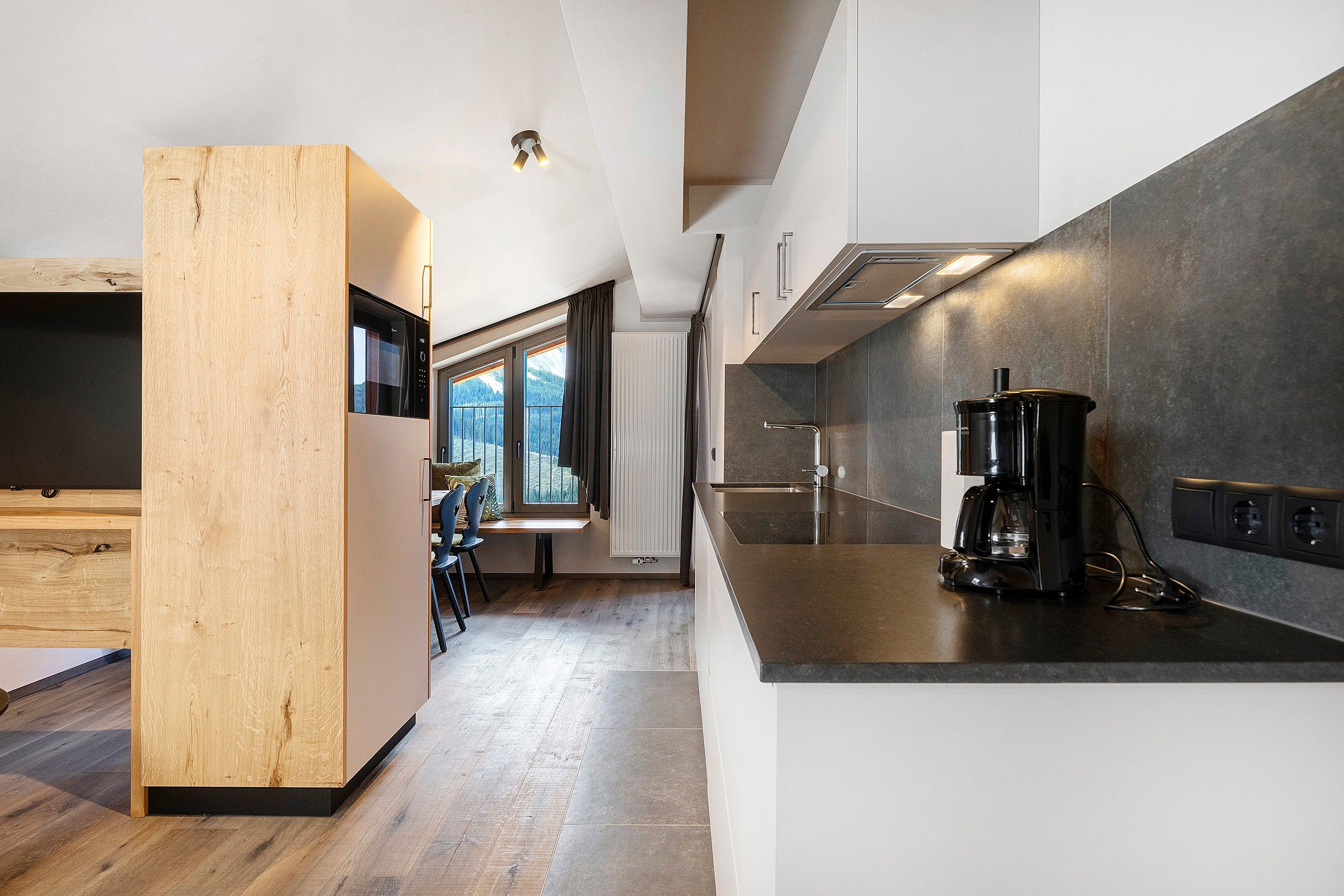 Eine moderne Küche mit integriertem Mikrowellenherd, einer Kaffeemaschine und Blick auf eine gebirgige Landschaft durch große Fenster.