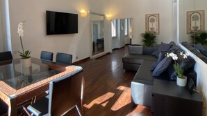 Un vaste espace de vie comprenant une table à manger, des chaises, un canapé et un téléviseur fixé au mur.